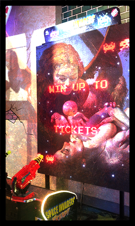 "Lilith and Eve" are now projected onto the wall of a video arcade, mostly on a scoreboard that says "WIN UP TO TICKETS." Without the butterfly, we can see an apple hovering over Lilith's hands, in the place where the number of tickets should be. In the bottom left is a laser gun and a label for Space Invaders.